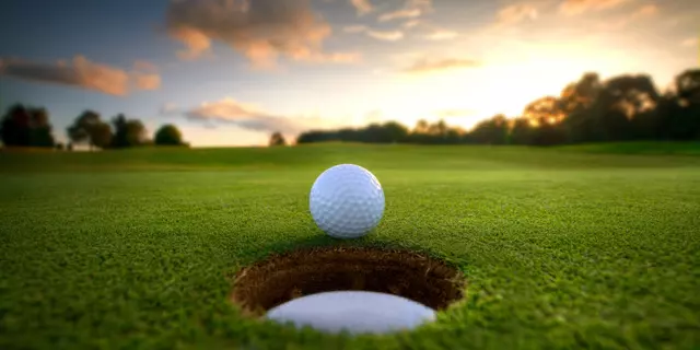 Golf ball about to fall into the cup at sunset