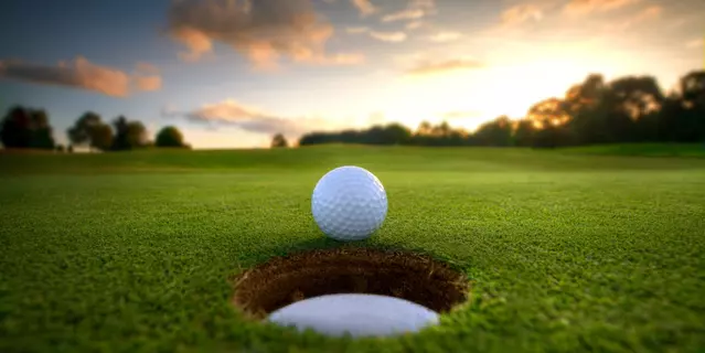 Golf ball about to fall into the cup at sunset