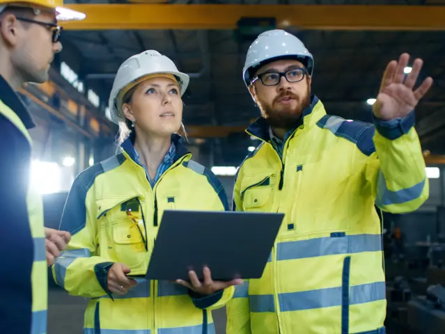 Male and Female Industrial Engineers Talk with Factory Worker while Using Laptop. They Work at the Heavy Industry Manufacturing Facility.