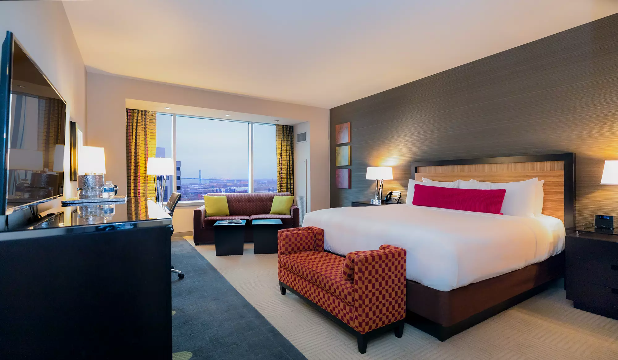 Gray room at MGM Grand Detroit with a queen-sized bed, couch, bedroom bench, desk and dresser.