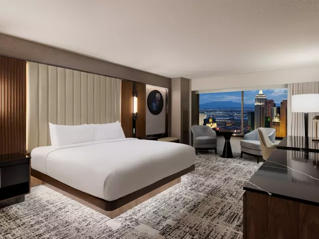 MGM Grand hotel bedroom with a large bed dressed in crisp white linens and a window overlooking the Las Vegas skyline.