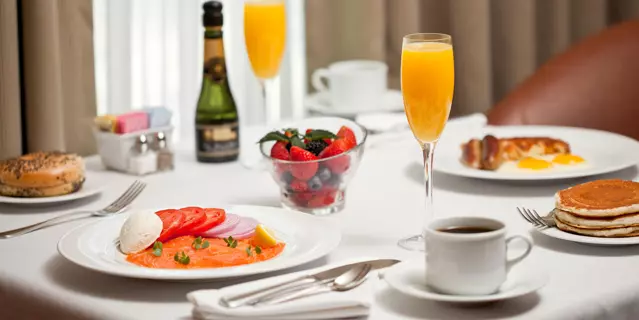 A breakfast featuring smoked salmon, pancakes, orange juice and champagne inside a room.