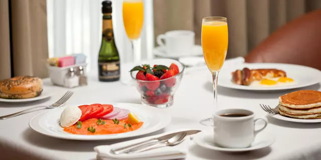 A breakfast featuring smoked salmon, pancakes, orange juice and champagne inside a room.