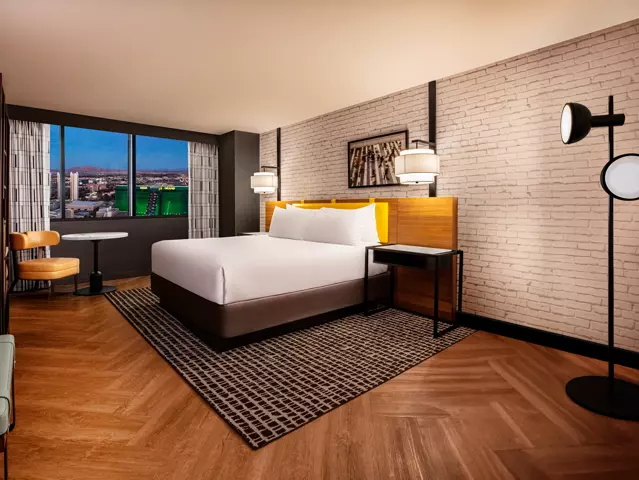 New York New York hotel bedroom with a large bed dressed in crisp white linens and a window overlooking the Las Vegas skyline.
