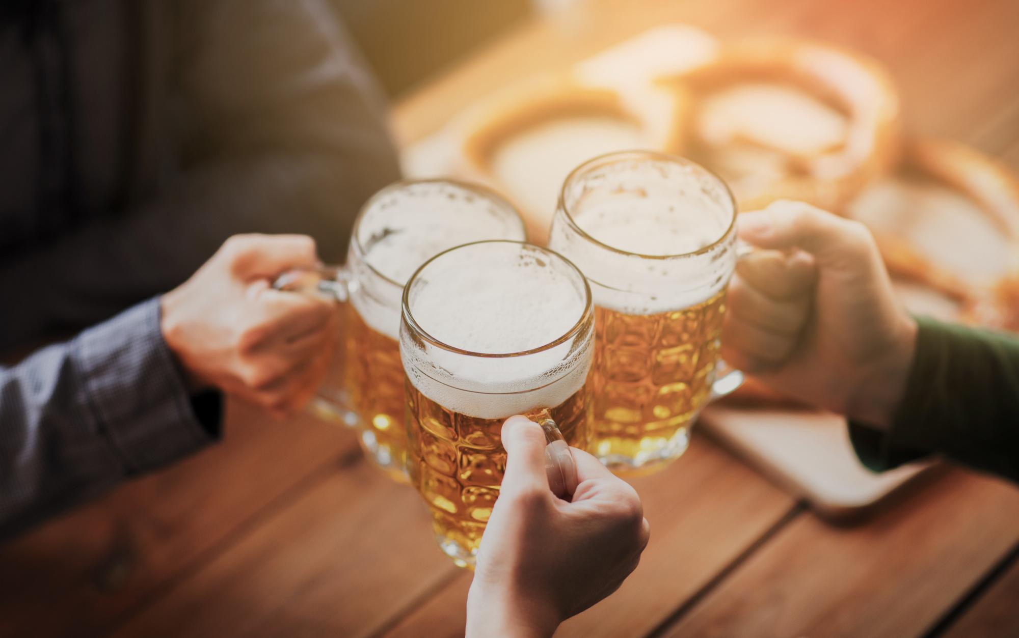 people, leisure and drinks concept - close up of hands clinking beer mugs at bar or pub