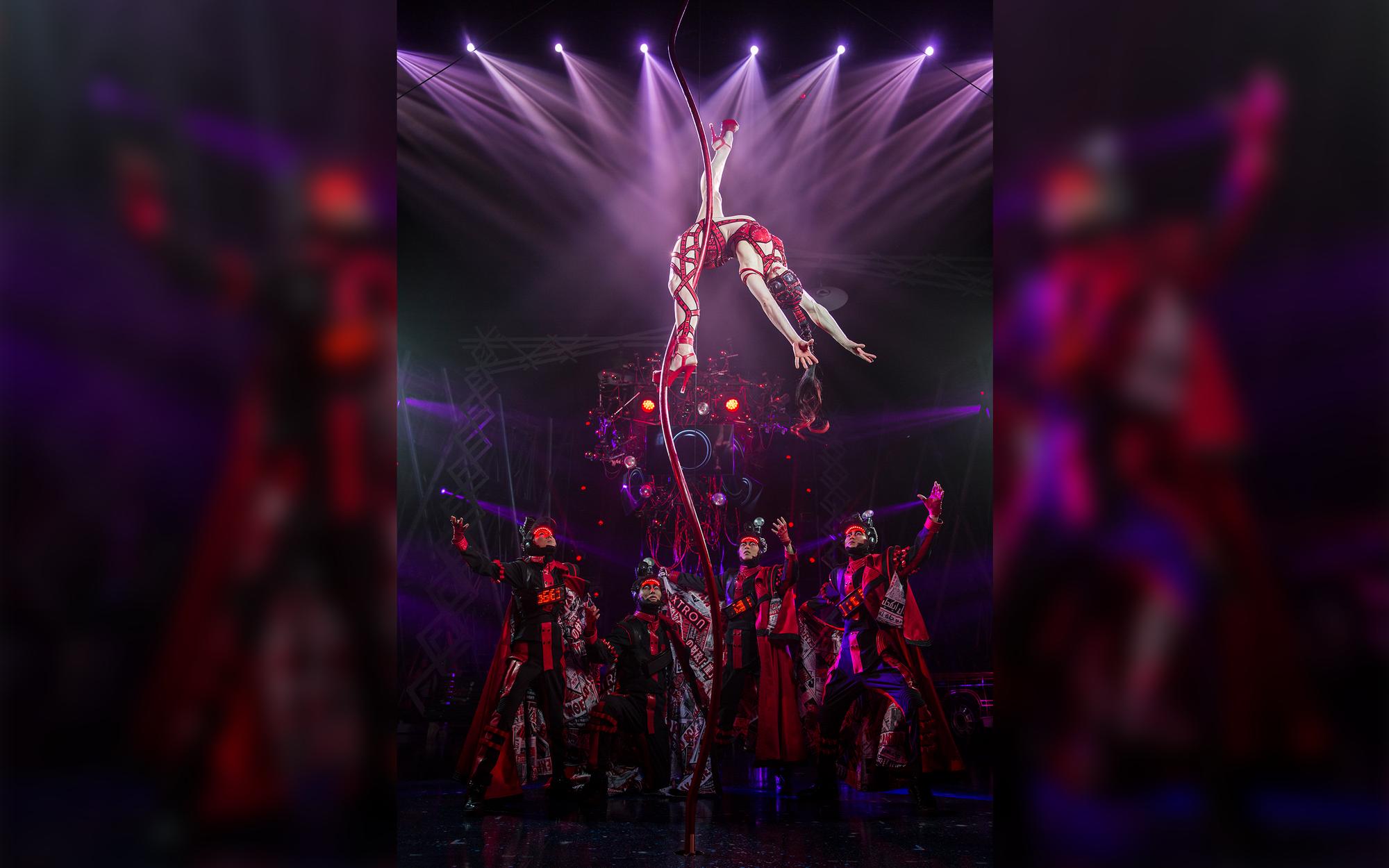 Woman hanging from rope above men looking up.