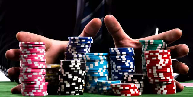 Gambler man hands pushing large stack of colored poker chips across gaming table for betting.