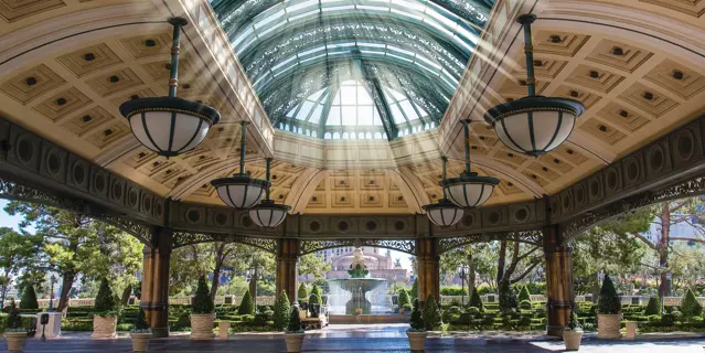 Covered entrance of the Bellagio with skylight windows in an open area, chandeliers and a water fountain in a garden.