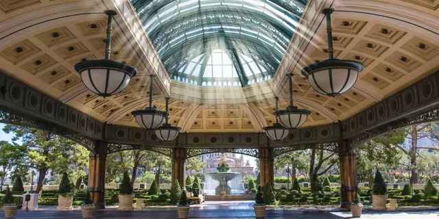 Covered entrance of the Bellagio with skylight windows in an open area, chandeliers and a water fountain in a garden.