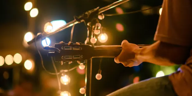 Rear view of the man sitting play acoustic guitar on the outdoor concert with a microphone stand in the front, musical concept.