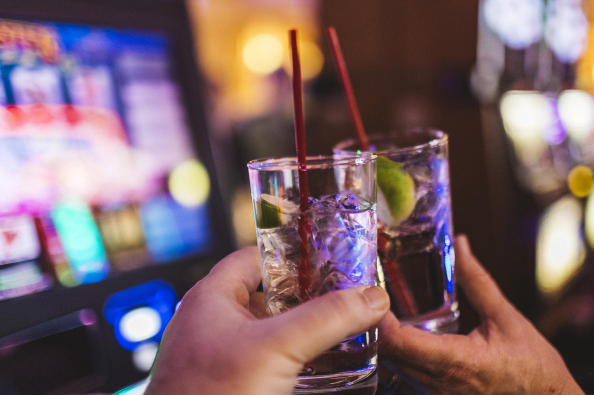 In a Las Vegas casino, cheering couple who just won big money at a slot machine. They each have a glass of gin and tonic in their hands. Faces are not visible