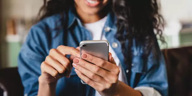 Cropped shot of a young woman using smart phone at home. Smiling woman using smartphone at home, messaging or browsing social networks while relaxing on couch