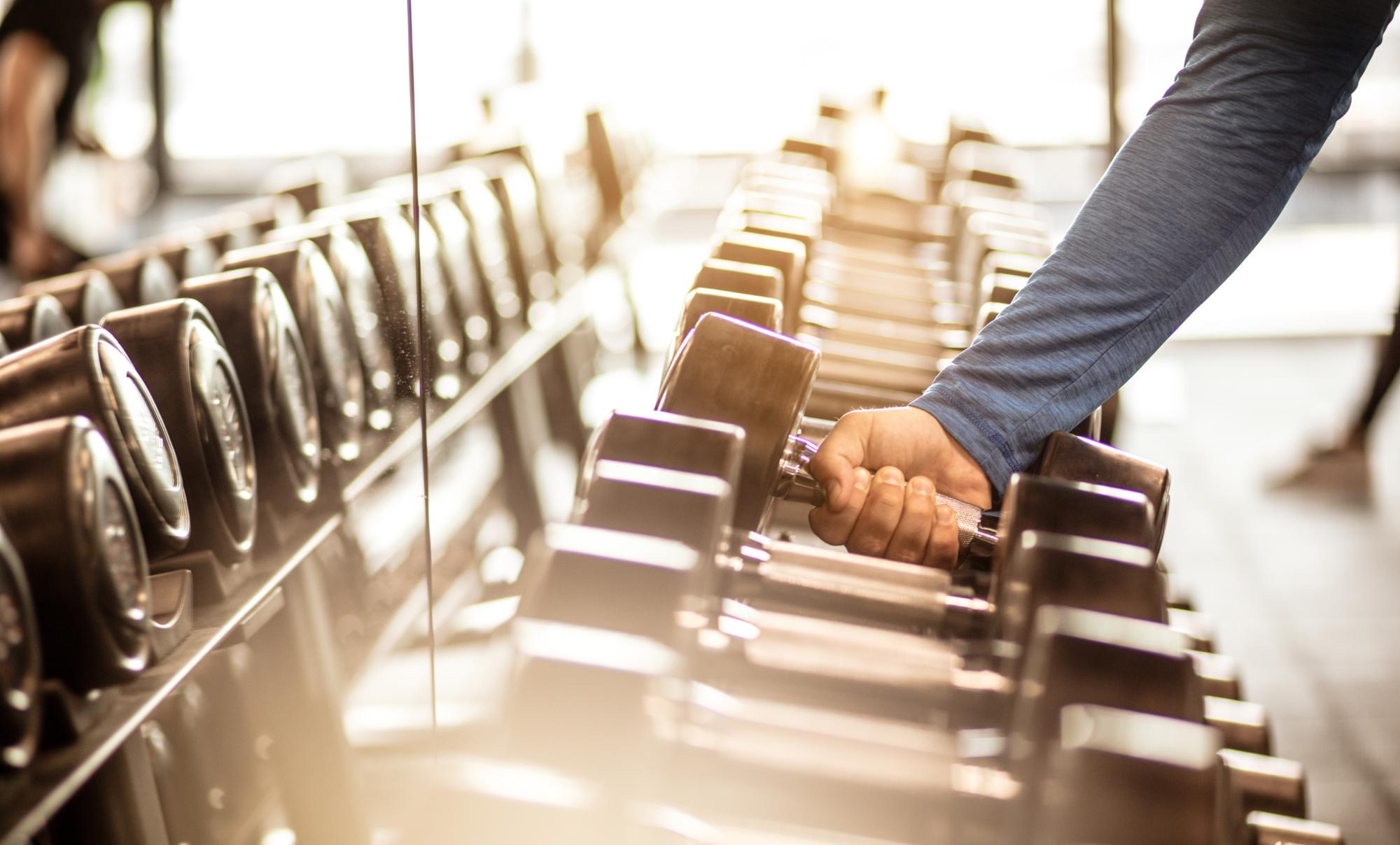 Time to pump that iron. Muscular build sportsman taking weights from a rack in a gym. Focus is on hand. Close up.