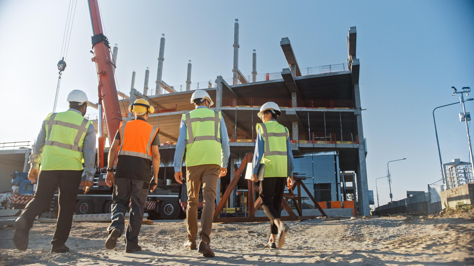 Diverse Team of Specialists Inspect Commercial, Industrial Building Construction Site. Real Estate Project with Civil Engineer, Investor and Businesswoman. In the Background Skyscraper Formwork Frames