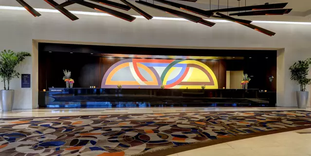 Reception of the Vdara at ARIA with a long desk, large colorful carpet and wooden light fixtures on the ceiling.