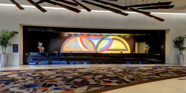 Reception of the Vdara at ARIA with a long desk, large colorful carpet and wooden light fixtures on the ceiling.