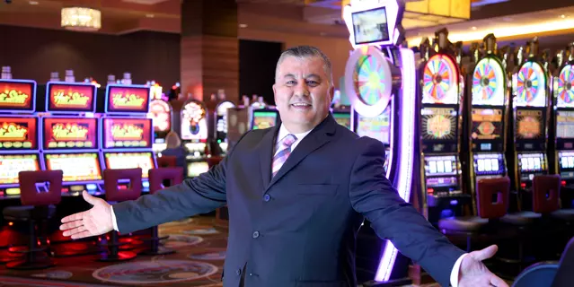 MGM Grand Detroit casino host Yassir Yasso standing in front of the slot machines inside the casino with his hands out.