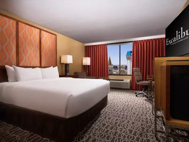Excalibur hotel bedroom with a large bed dressed in crisp white linens and a window overlooking the Las Vegas skyline.