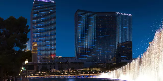 Exterior view of The Cosmopolitan hotel with a the Bellagio water fountains at night.