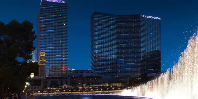 Exterior of The Cosmopolitan of Las Vegas at night shows two buildings with 40 floors each in front a lake with fountains.