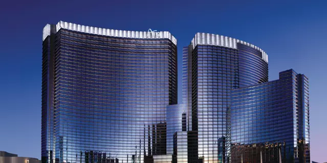 Exterior of ARIA with two thin curved buildings of mirrored glass with 28 floors each and a fountain with colored lights in front.