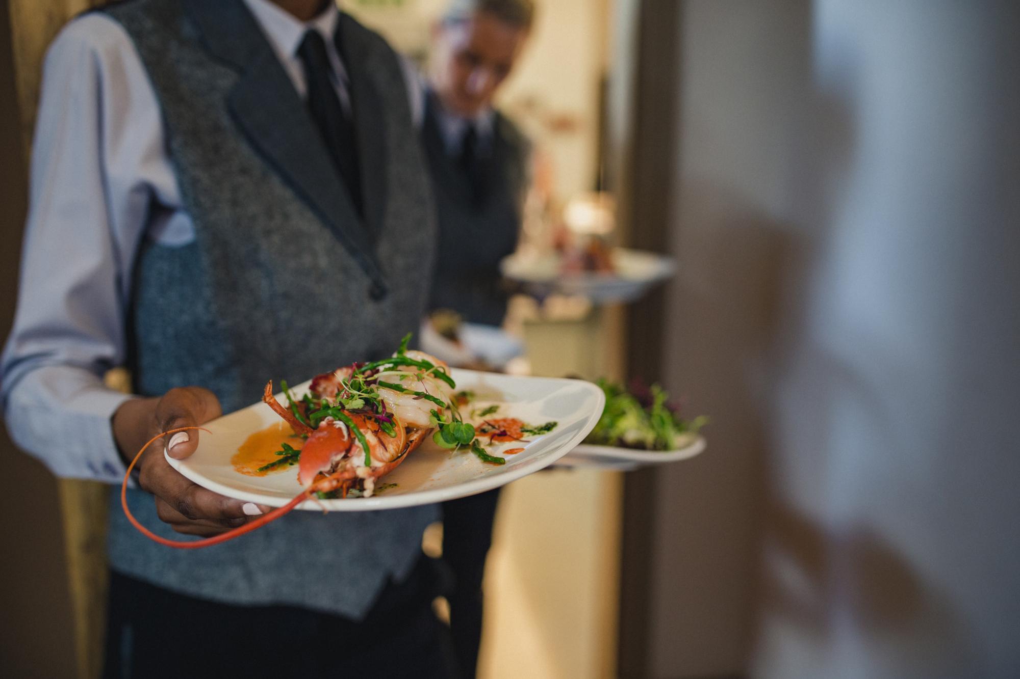 Two unrecognisable waiters are coming out of a hotel kitchen while holding two dishes each, ready to serve to guests.