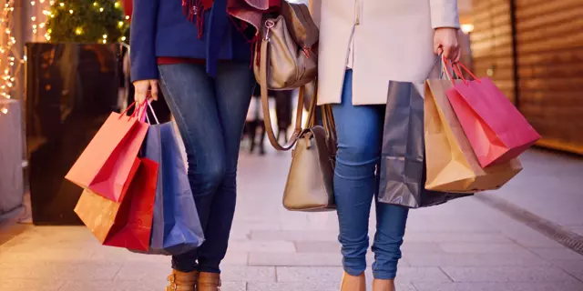 Young women shopping in the city, legs and hands close up, carrying paper bags.