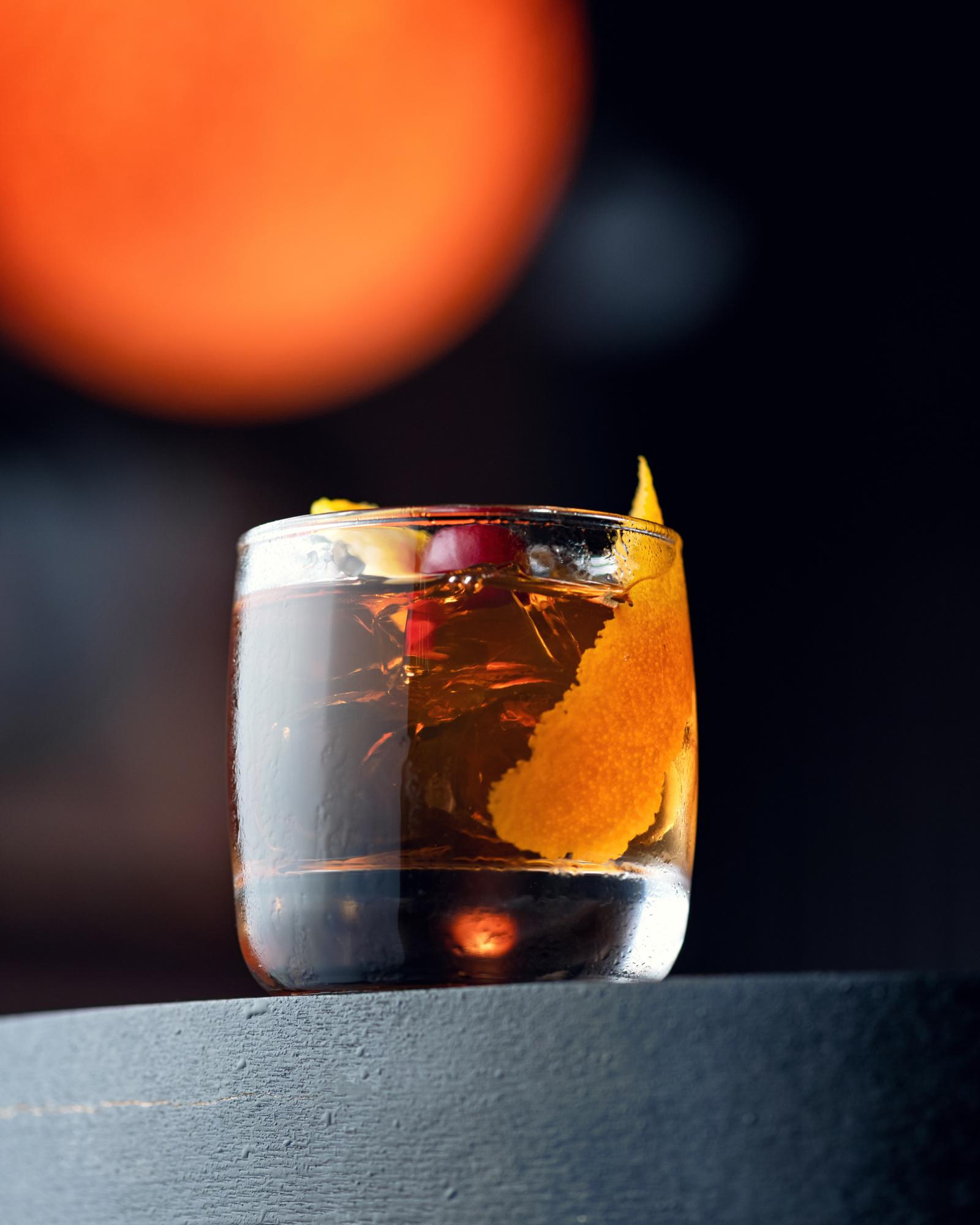 Strong Alcoholic drink or cocktail. Glass of cold Rum with ice and citrus on a black background with beautiful bokeh. Close up shot. Soft focus. Square format with copy space for text.
