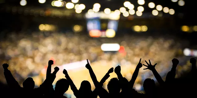 Fans excited at basketball game. Silhouetted fans raising arms in celebration at a basketball game.