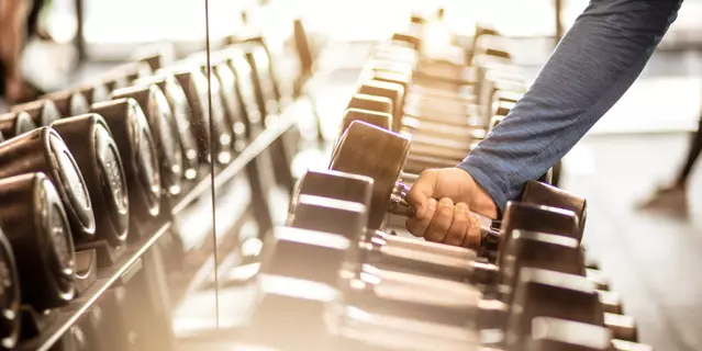 Time to pump that iron. Muscular build sportsman taking weights from a rack in a gym. Focus is on hand. Close up.