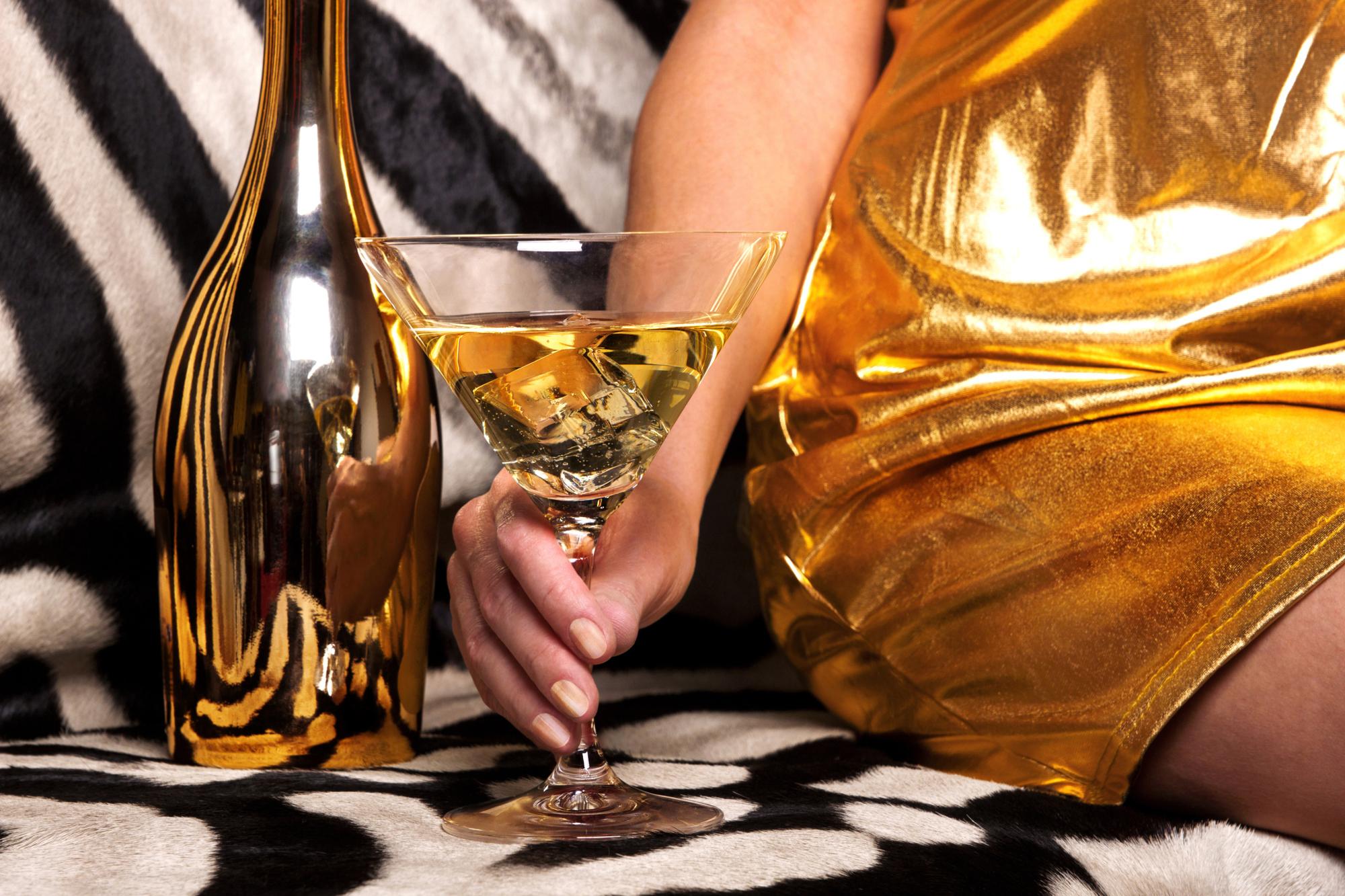 Beautiful woman in gold drinks a cocktail on a rich background. A female hand holds a glass with a martini on the background of a zebra skin.