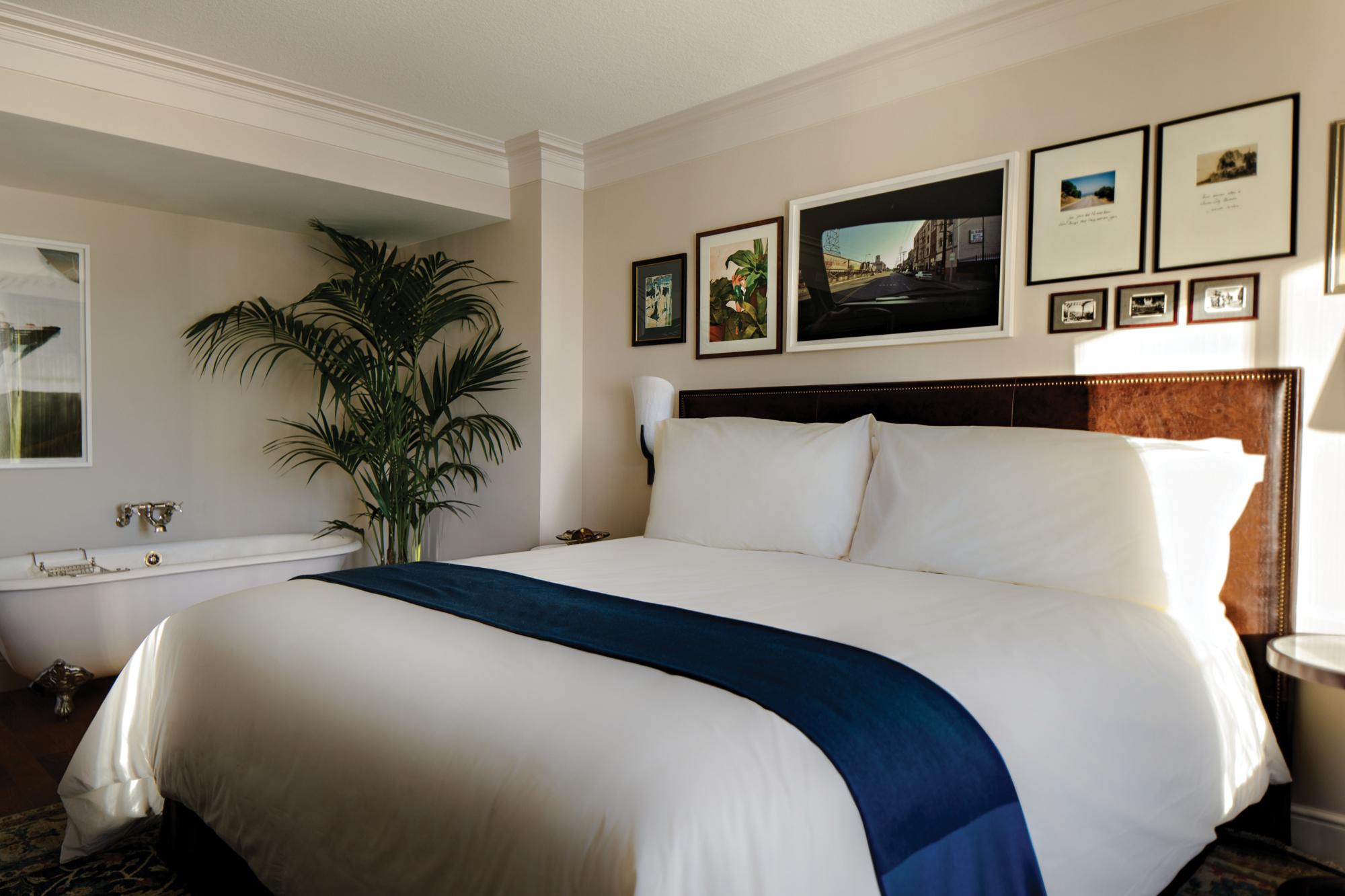 White room at The Reserve at Park MGM decorated with a queen-sized bed, small palm tree and old-fashioned bathtub with a rounded top edge, that stands on four feet.