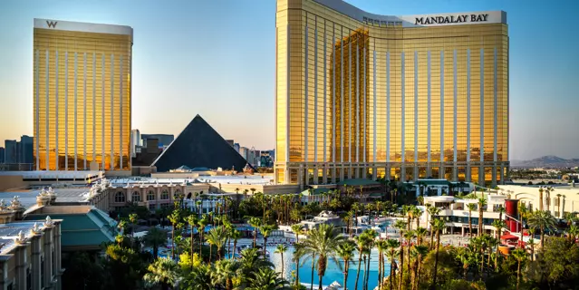 Exterior of Mandalay Bay shows a bending gold glass building with 36 floors and pools surrounded by palm trees in front.