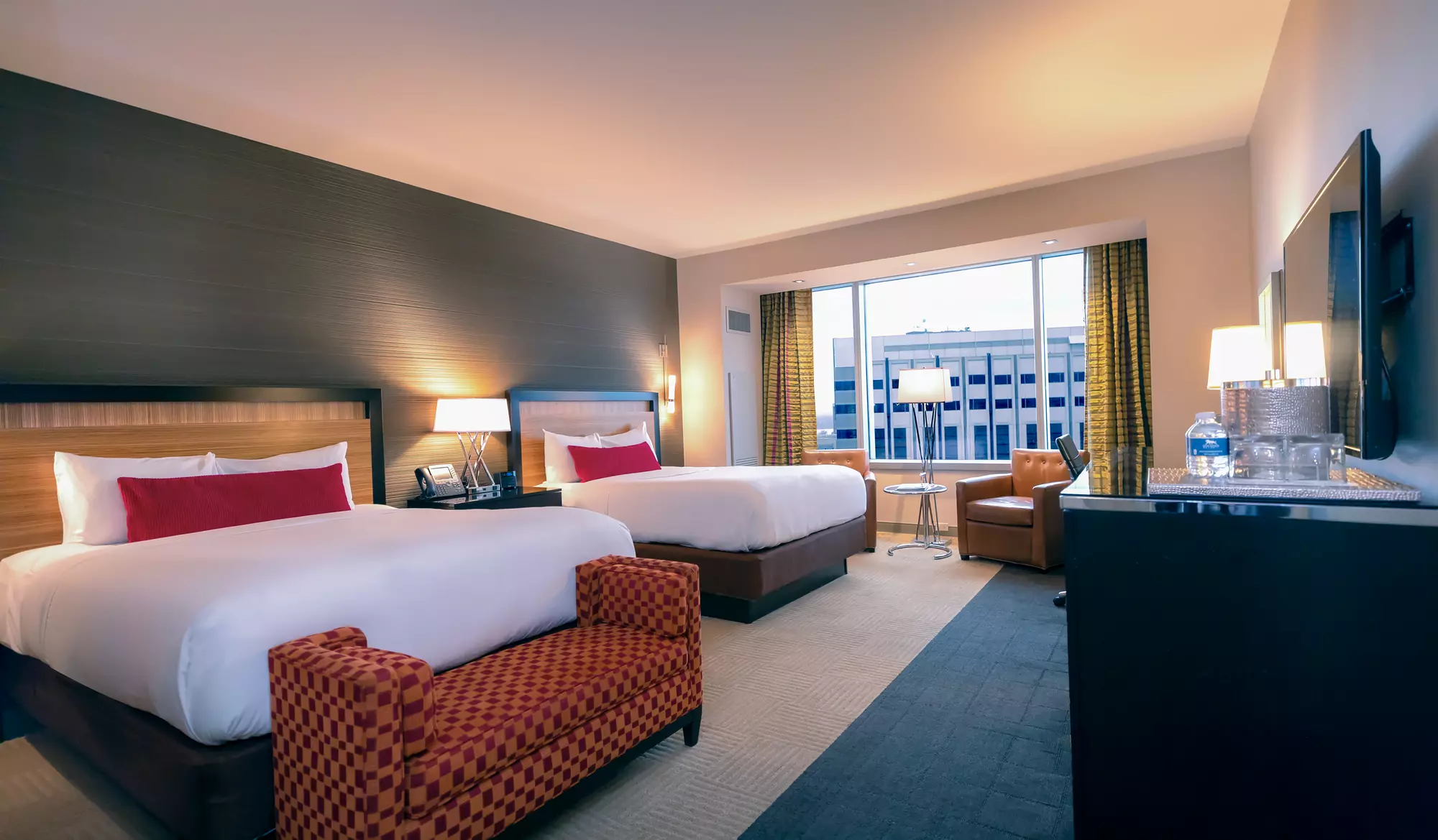 Larger gray room at MGM Grand Detroit with 2 queen-sized beds, 2 cushioned chairs, a bedroom bench, desk and dresser.