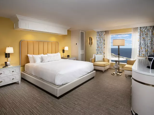 Yellow room at the Beau Rivage with a king-sized bed, 2 cushioned chairs, television and window with a bay view.