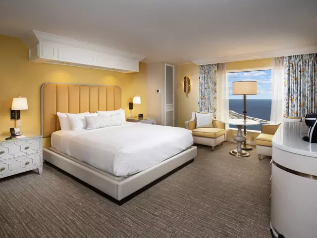 Yellow room at the Beau Rivage with a king-sized bed, 2 cushioned chairs, television and window with a bay view.