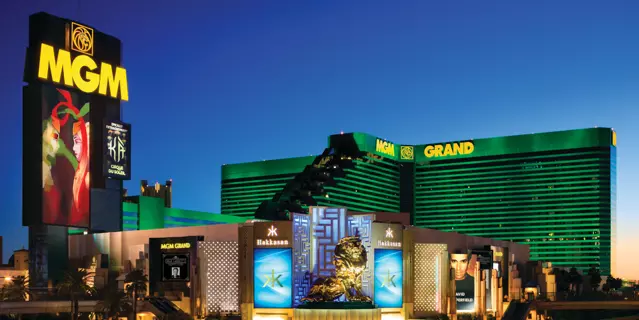 Exterior of the MGM Grand Las Vegas shows a green, glass, L-shaped building with 29 floors with the casino and gold statue of the MGM lion in front.
