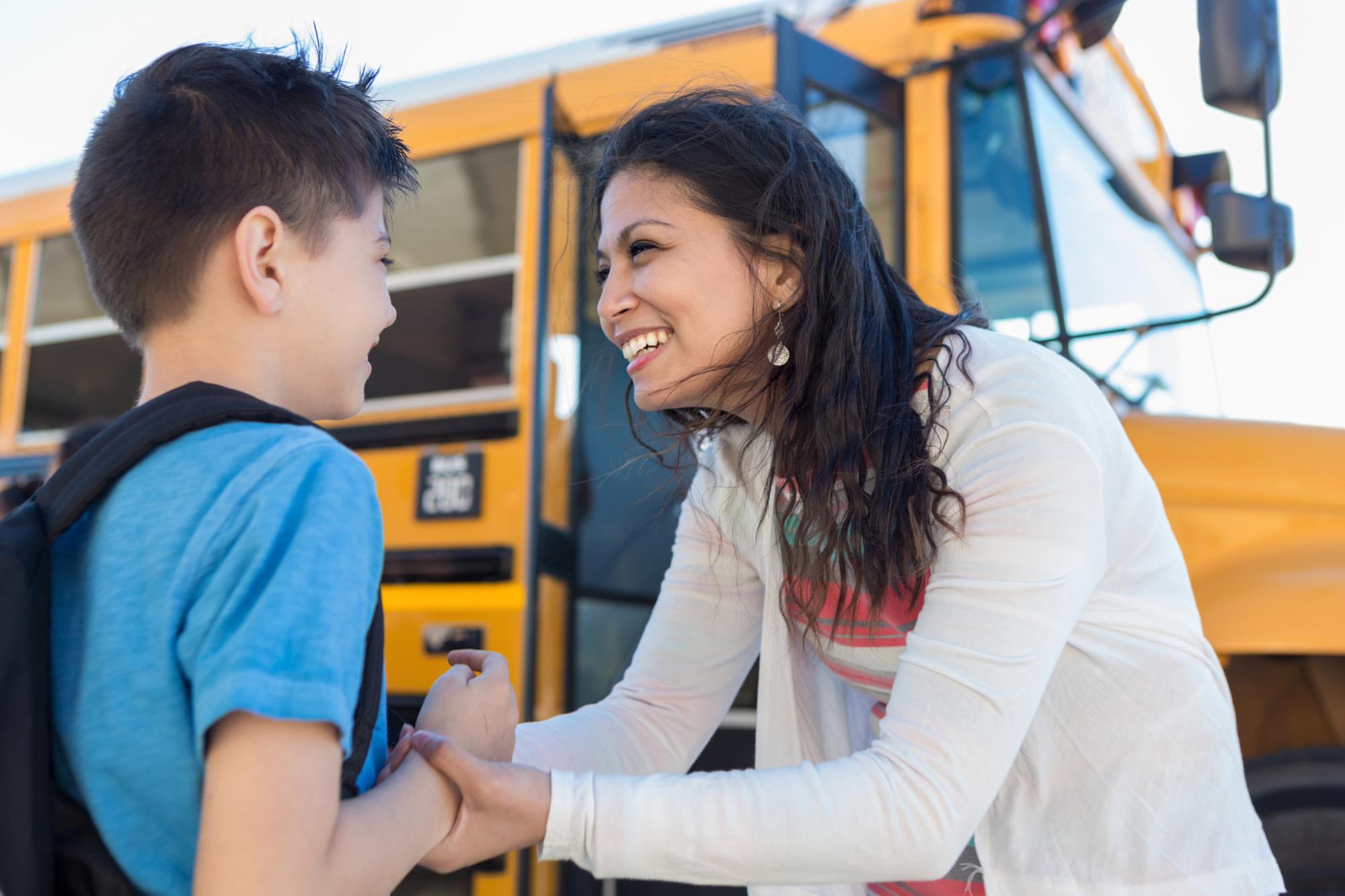 As they stand by the bus, the mid adult mom encourages her young son on the first day of school.