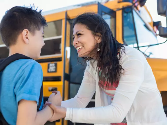 As they stand by the bus, the mid adult mom encourages her young son on the first day of school.