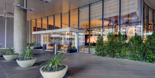 Covered, glass entrance of the Vdara at ARIA with big potted trees and large pillars.