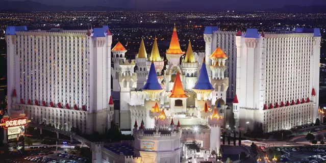 Exterior of Excalibur shows two large white buildings with 28 floors and 11 castle-like towers in the between the two buildings with a sunset mountain view.
