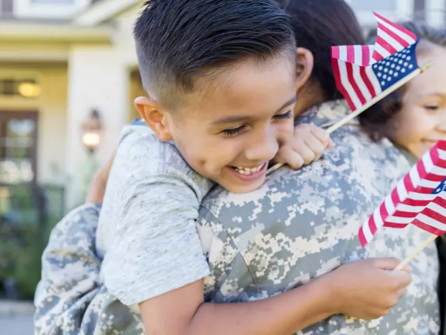 Smiling little boy and girl give their soldier mom a big hug on her return home from service. The children are holding small US flags.