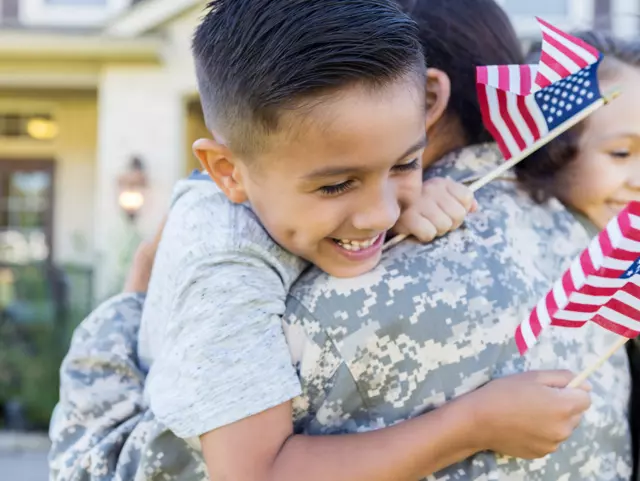 Smiling little boy and girl give their soldier mom a big hug on her return home from service. The children are holding small US flags.